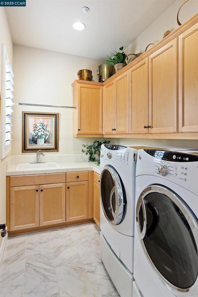 clothes washing area with cabinets, washing machine and dryer, and sink