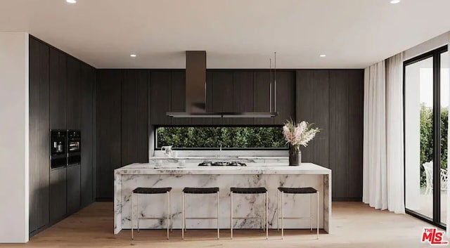 kitchen with light wood-type flooring, a center island, wall chimney exhaust hood, and a breakfast bar area