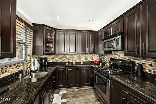 kitchen with dark brown cabinets, stainless steel appliances, sink, dark stone countertops, and light hardwood / wood-style floors