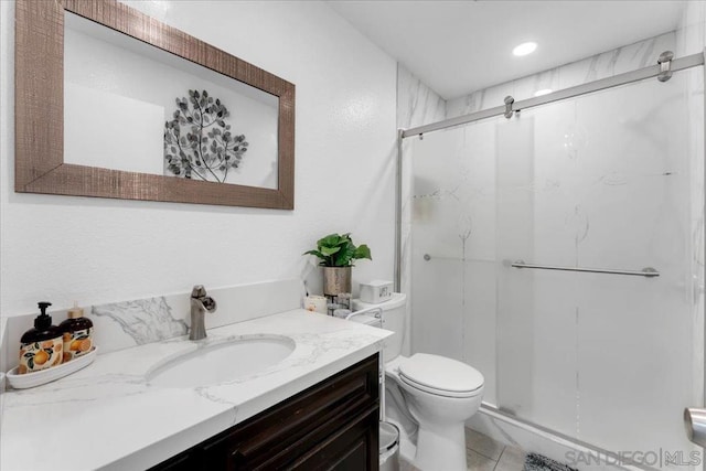 bathroom with a shower with door, vanity, tile patterned flooring, and toilet