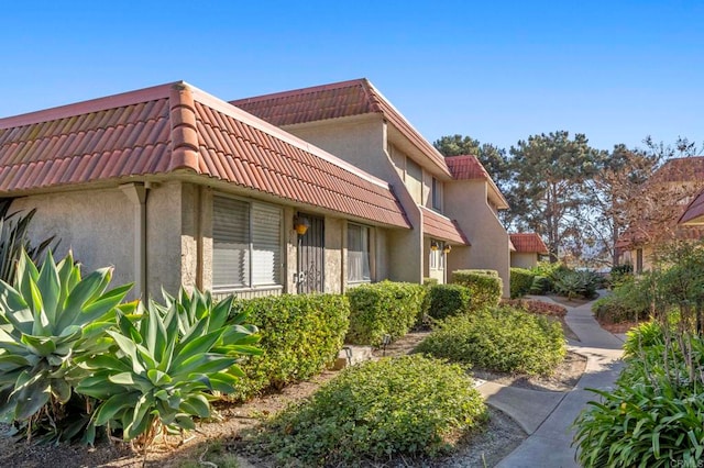 view of side of home with mansard roof, a tile roof, and stucco siding