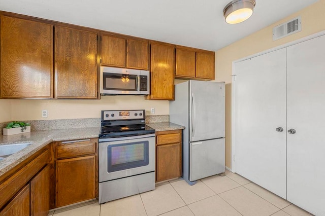 kitchen with appliances with stainless steel finishes, light tile patterned flooring, visible vents, and brown cabinets