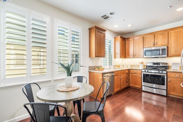 kitchen with sink, stainless steel appliances, light stone counters, and dark wood-type flooring