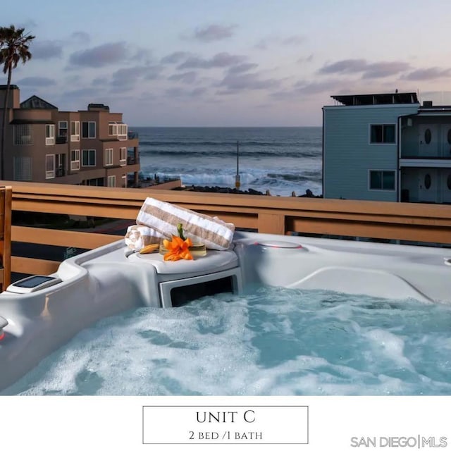 pool at dusk featuring a water view and a hot tub