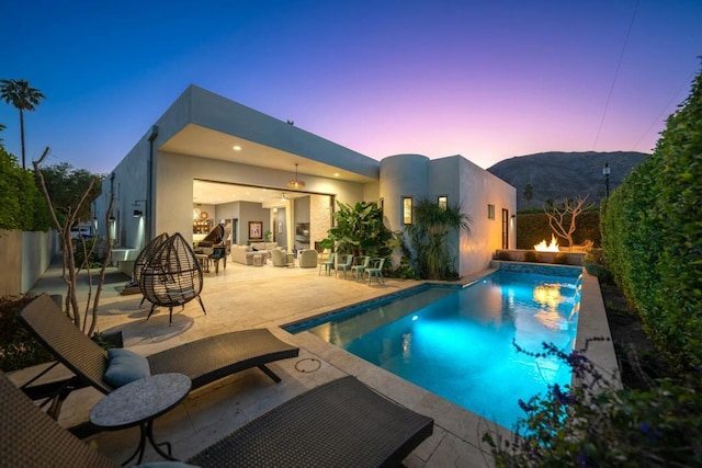 pool at dusk with a patio area, ceiling fan, pool water feature, and a mountain view