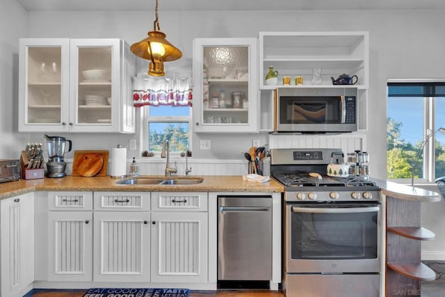 kitchen featuring white cabinetry, sink, light stone countertops, decorative light fixtures, and appliances with stainless steel finishes