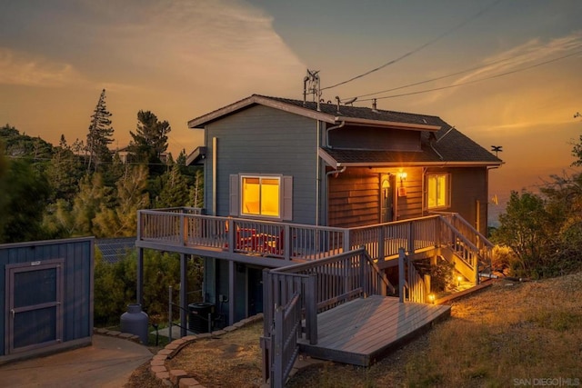 back house at dusk featuring a shed, a deck, and central AC unit