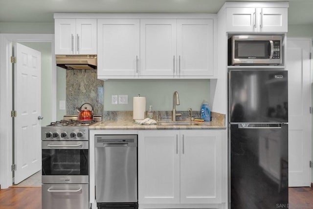 kitchen with light stone countertops, stainless steel appliances, sink, exhaust hood, and white cabinets