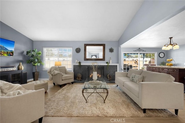 living room with a brick fireplace, vaulted ceiling, light hardwood / wood-style flooring, and plenty of natural light