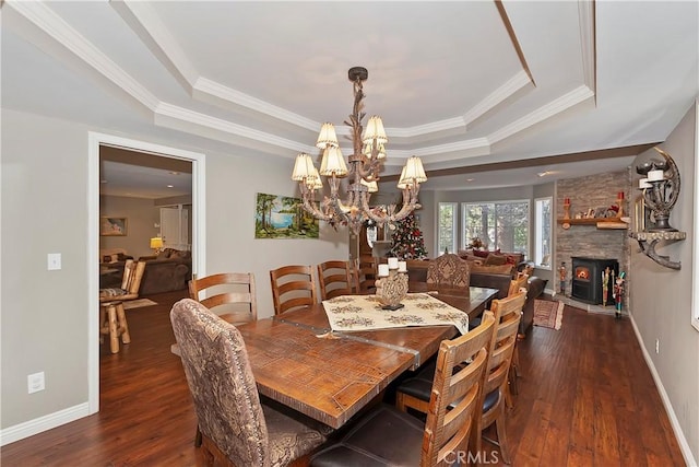 dining area featuring an inviting chandelier, a fireplace, ornamental molding, dark hardwood / wood-style flooring, and a raised ceiling