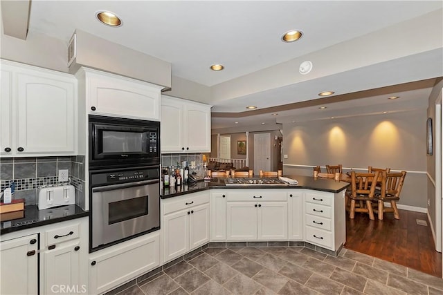 kitchen featuring kitchen peninsula, backsplash, stainless steel appliances, and white cabinetry