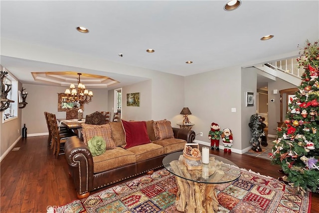 living room featuring a notable chandelier, a tray ceiling, and dark wood-type flooring