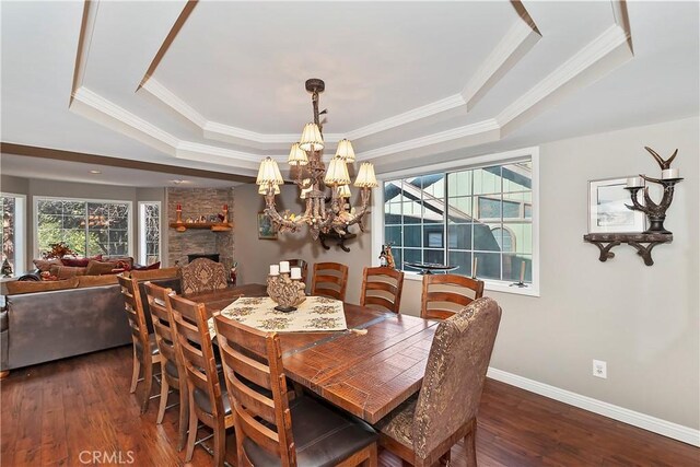 dining space with dark wood-type flooring, a raised ceiling, a chandelier, a fireplace, and ornamental molding