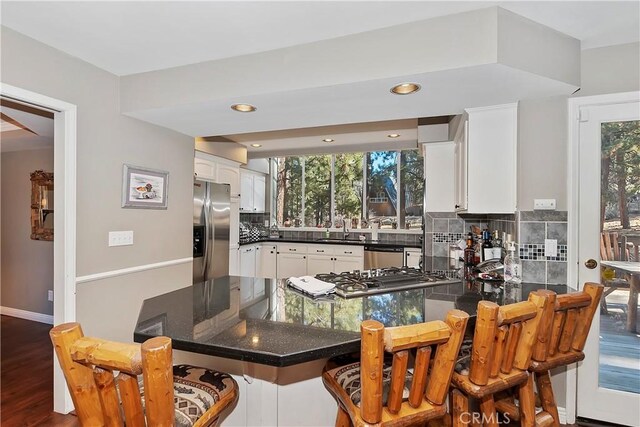 kitchen featuring sink, kitchen peninsula, decorative backsplash, white cabinets, and appliances with stainless steel finishes