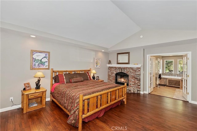 bedroom featuring hardwood / wood-style flooring, vaulted ceiling, a brick fireplace, and ensuite bath