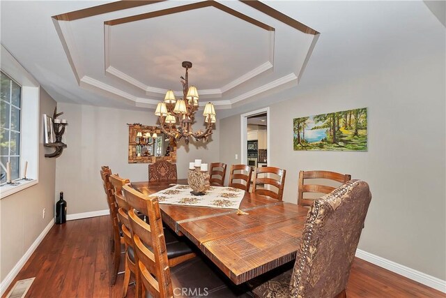 dining room with a tray ceiling, crown molding, dark wood-type flooring, and a notable chandelier