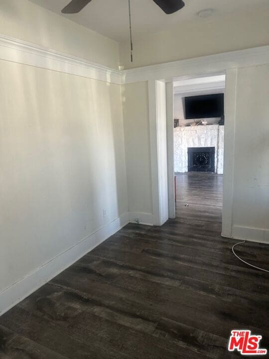 interior space featuring a fireplace, ceiling fan, and dark wood-type flooring