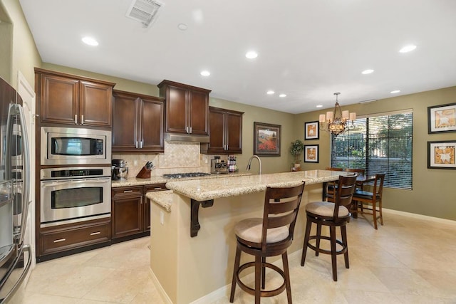 kitchen featuring a kitchen island with sink, decorative light fixtures, appliances with stainless steel finishes, a notable chandelier, and a kitchen bar