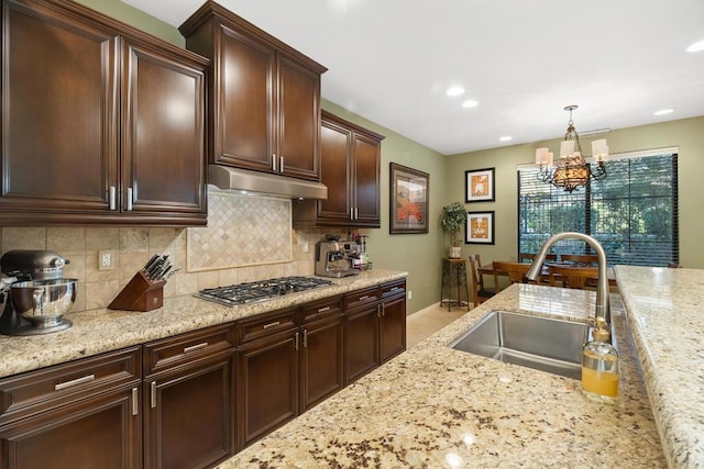 kitchen with light stone countertops, sink, hanging light fixtures, a chandelier, and stainless steel gas stovetop