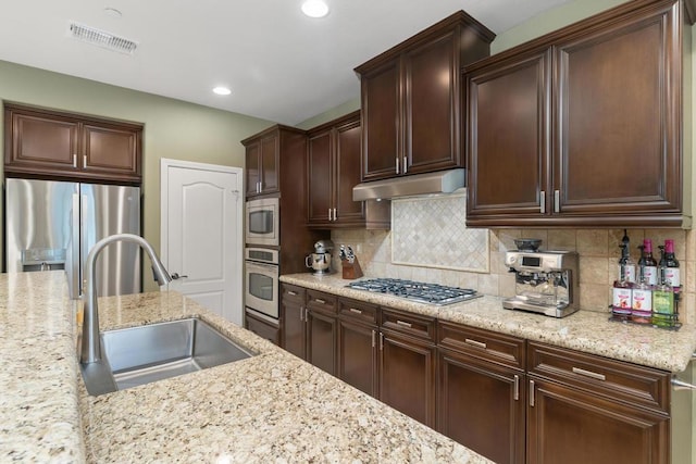 kitchen featuring light stone countertops, appliances with stainless steel finishes, backsplash, dark brown cabinetry, and sink