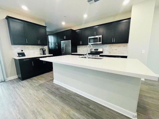 kitchen featuring a center island with sink, appliances with stainless steel finishes, light hardwood / wood-style floors, and sink