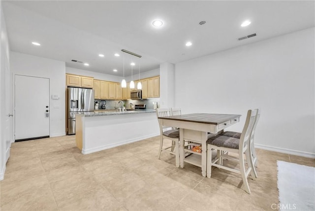 kitchen with light brown cabinets, hanging light fixtures, appliances with stainless steel finishes, tasteful backsplash, and light stone counters