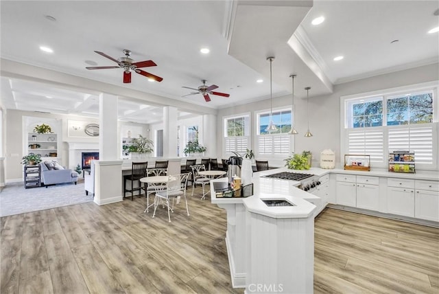 kitchen featuring light wood-type flooring, ceiling fan, crown molding, white cabinetry, and hanging light fixtures