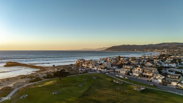 aerial view at dusk with a water and mountain view and a view of the beach