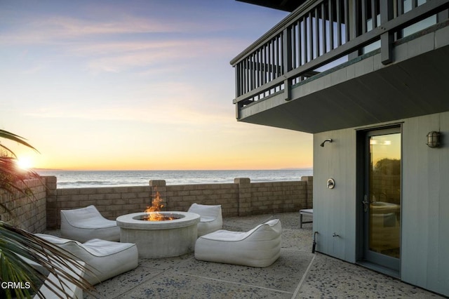 patio terrace at dusk featuring an outdoor fire pit, a balcony, and a water view