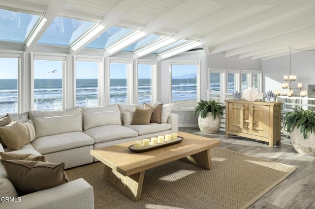 sunroom featuring a beach view, a water view, lofted ceiling with beams, and a chandelier