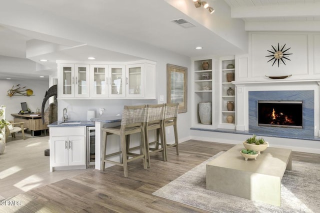 bar featuring white cabinets, a fireplace, beamed ceiling, light hardwood / wood-style floors, and built in features