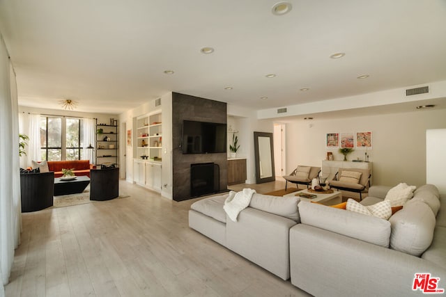 living room featuring a fireplace, built in shelves, and light hardwood / wood-style flooring