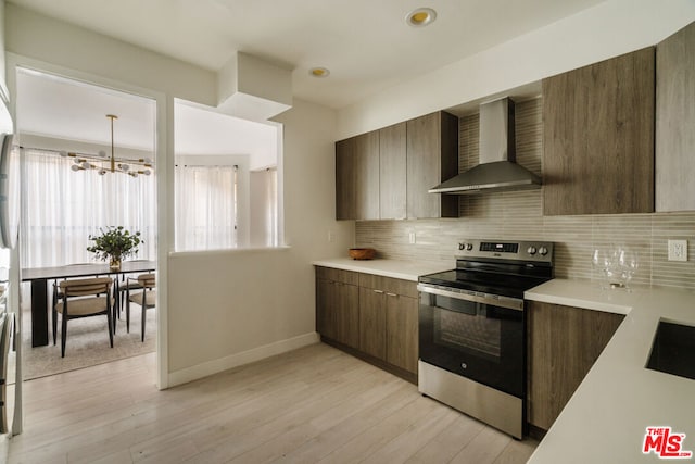 kitchen with light wood-type flooring, backsplash, stainless steel range with electric stovetop, wall chimney exhaust hood, and a notable chandelier