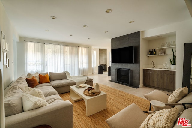 living room featuring light wood-type flooring, wet bar, and a tiled fireplace