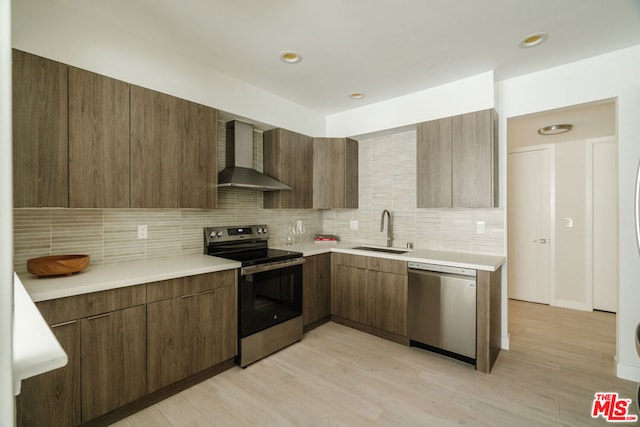 kitchen featuring sink, wall chimney exhaust hood, stainless steel appliances, light hardwood / wood-style floors, and decorative backsplash