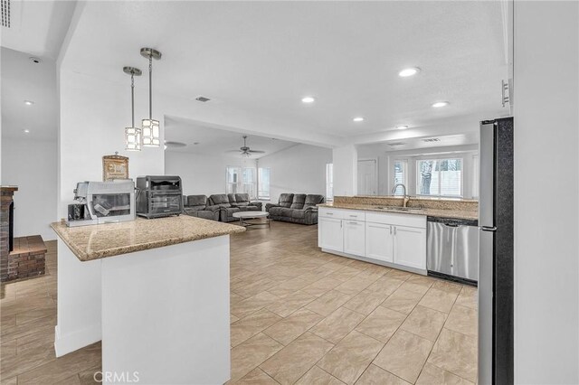 kitchen featuring light stone counters, stainless steel appliances, sink, decorative light fixtures, and white cabinetry