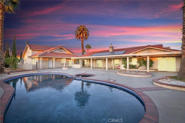 pool at dusk with an in ground hot tub and a patio area