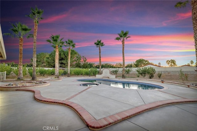 pool at dusk with a hot tub and a patio area