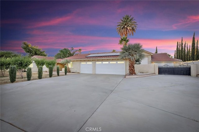 ranch-style home with a garage, fence, driveway, roof mounted solar panels, and stucco siding