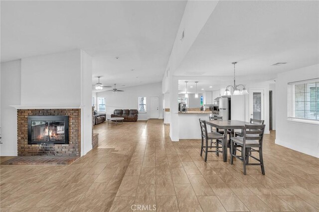 dining space featuring a fireplace, ceiling fan with notable chandelier, vaulted ceiling, and a healthy amount of sunlight