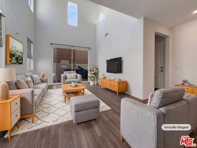 living room featuring a wealth of natural light, a towering ceiling, and dark hardwood / wood-style floors