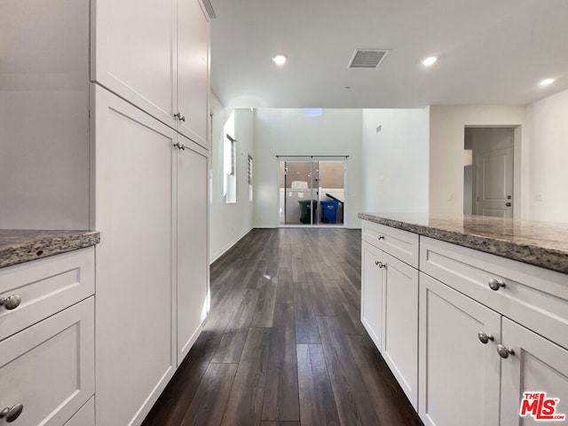 kitchen featuring dark wood-type flooring, dark stone countertops, and white cabinets