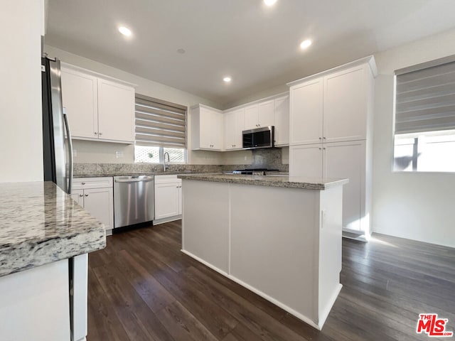 kitchen with appliances with stainless steel finishes, dark hardwood / wood-style flooring, a kitchen island, white cabinets, and light stone counters