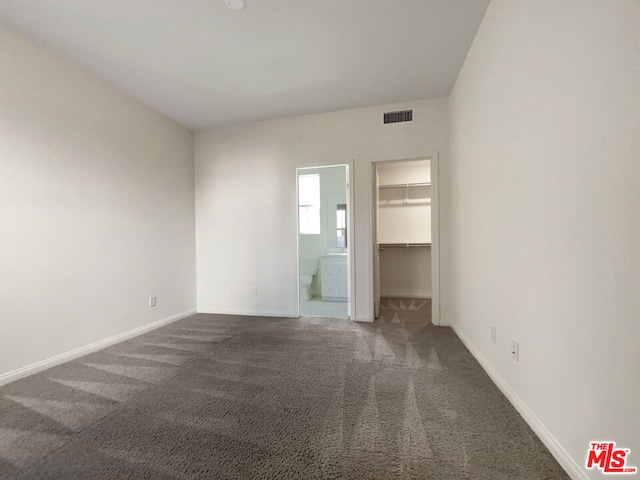 unfurnished bedroom with a spacious closet, dark carpet, ensuite bathroom, and a closet