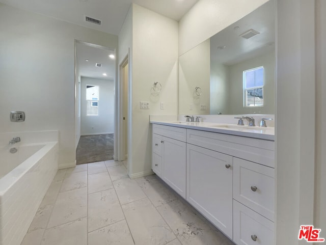 bathroom with tiled bath, vanity, and a healthy amount of sunlight