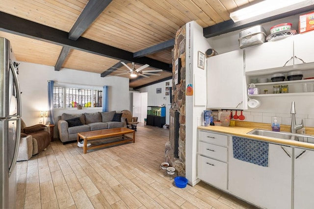 kitchen featuring beam ceiling, stainless steel fridge, white cabinetry, and sink