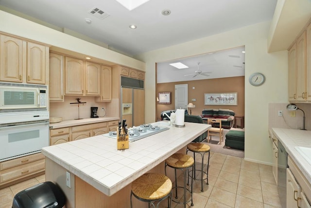 kitchen with tile countertops, a center island, a skylight, built in appliances, and ceiling fan