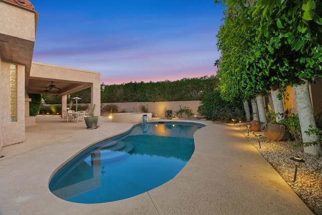 pool at dusk featuring ceiling fan and a patio