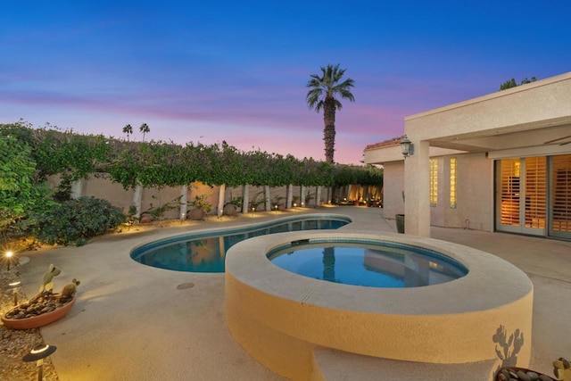 pool at dusk featuring an in ground hot tub and a patio