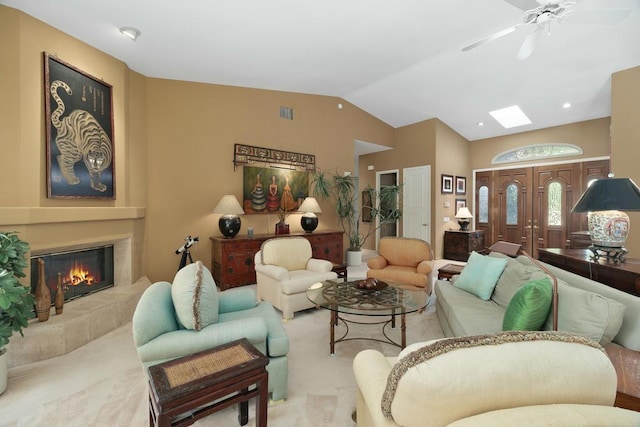 living room featuring a tile fireplace, ceiling fan, vaulted ceiling with skylight, and light colored carpet